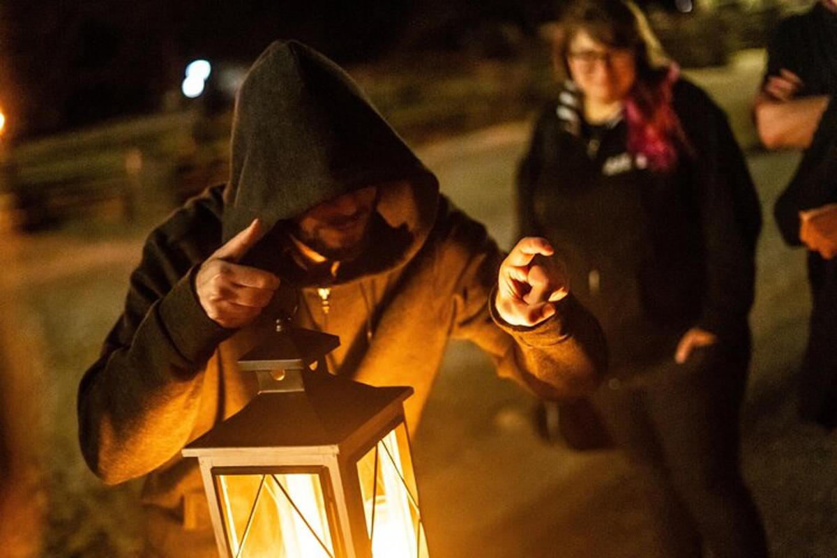 a man in a hood holding onto a lantern at night