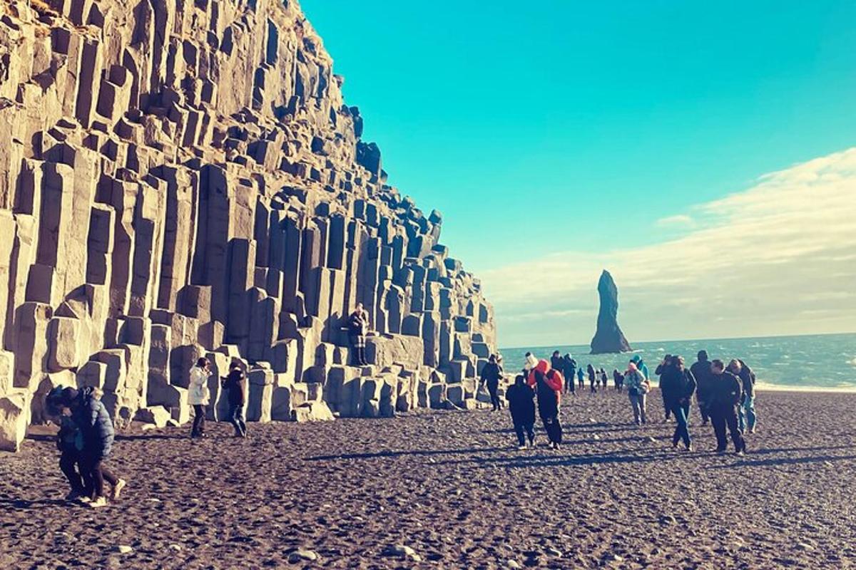 sekumpulan orang berjalan di pantai di sebelah dinding batu