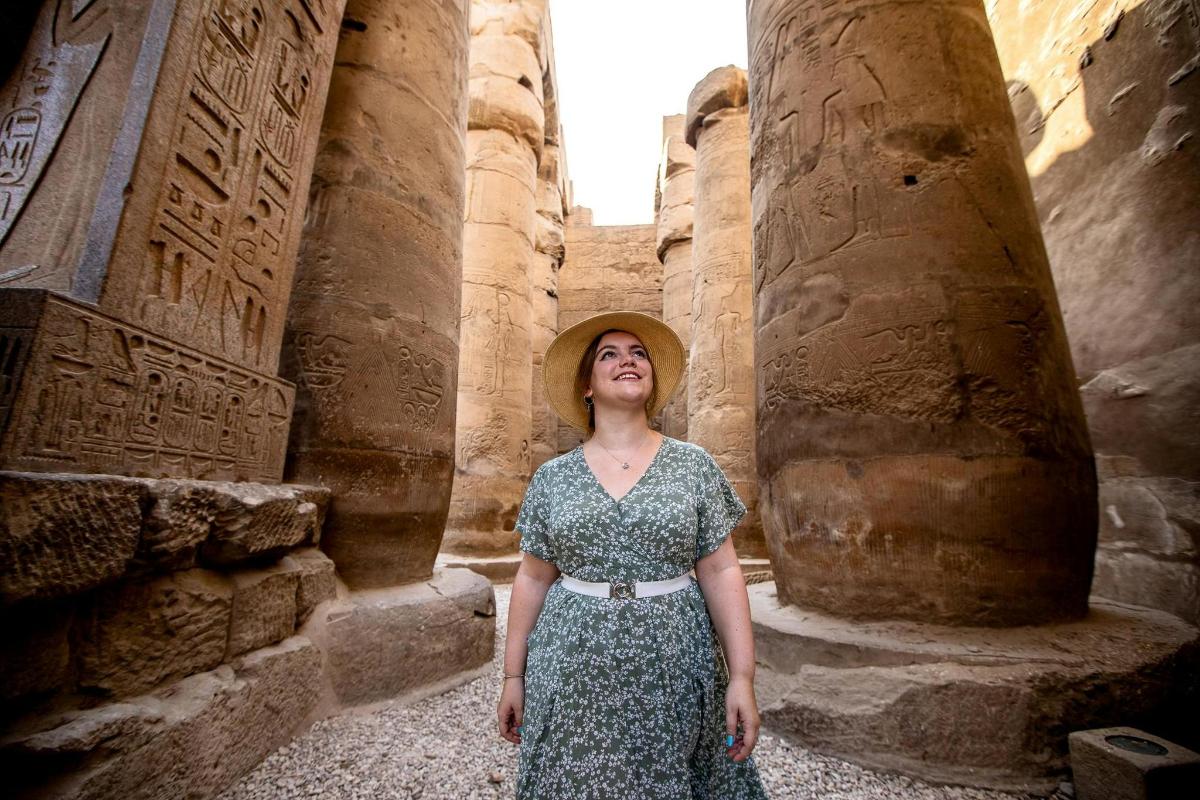 una donna che indossa un cappello in piedi tra antiche rovine