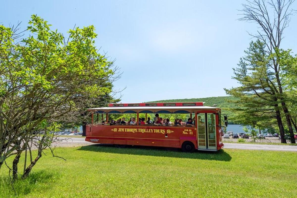 a red trolley bus filled with passengers in a field