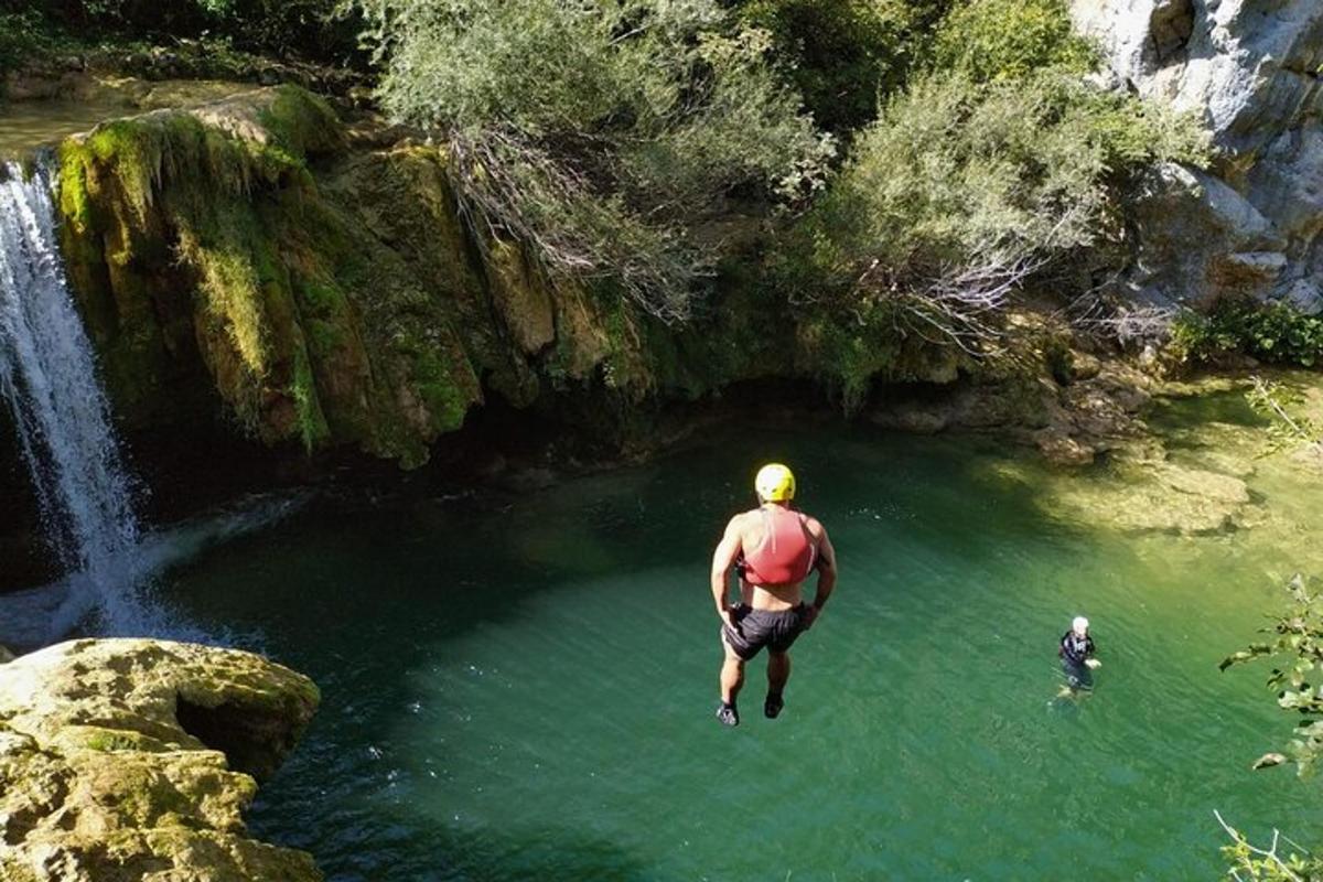 a man jumping into a pool of water near a waterfall