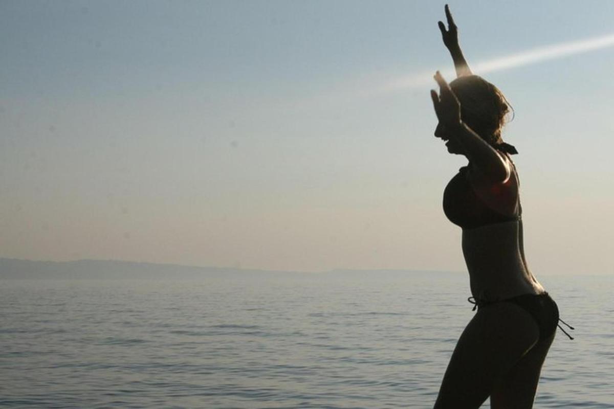 μια γυναίκα που στέκεται δίπλα στο νερό με τα χέρια της ψηλά