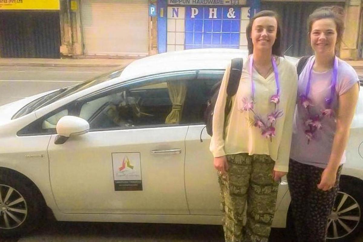 two women standing in front of a white car