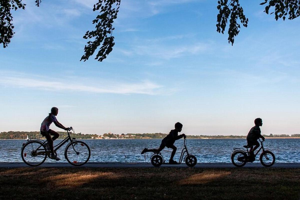 tres persones anant en bicicleta per un camí vora l'aigua