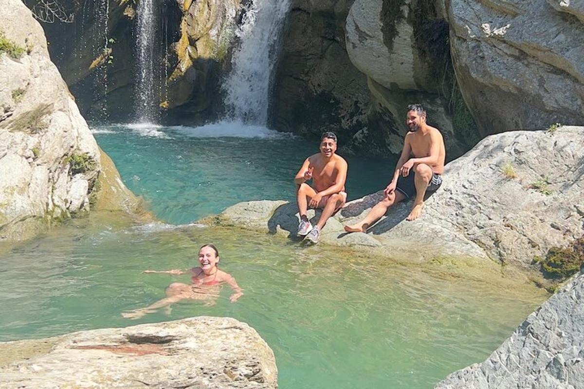 três homens sentados em uma piscina ao lado de uma cachoeira