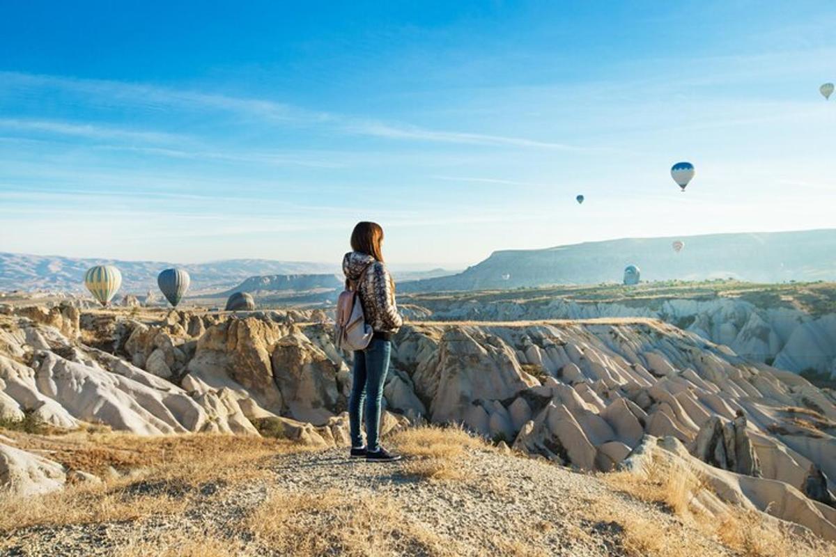 seorang wanita berdiri di atas bukit melihat belon udara panas