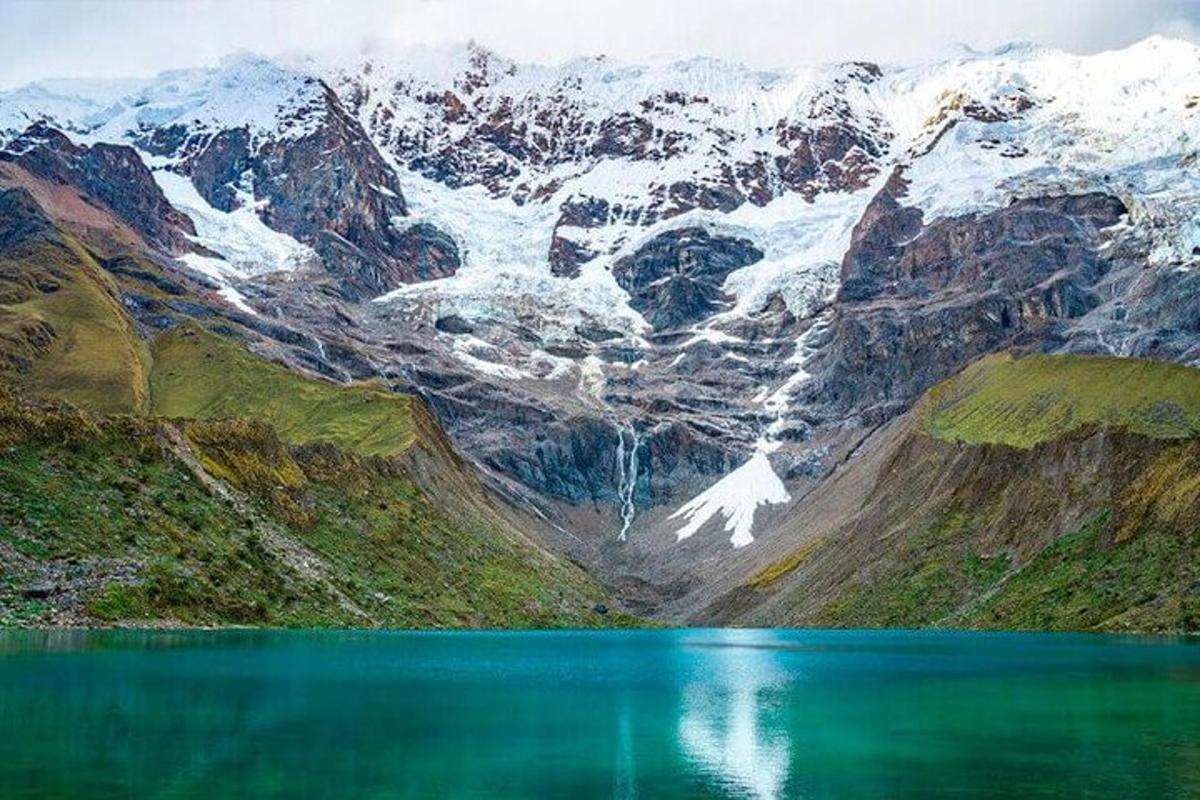 Una montaña con un lago verde enfrente.
