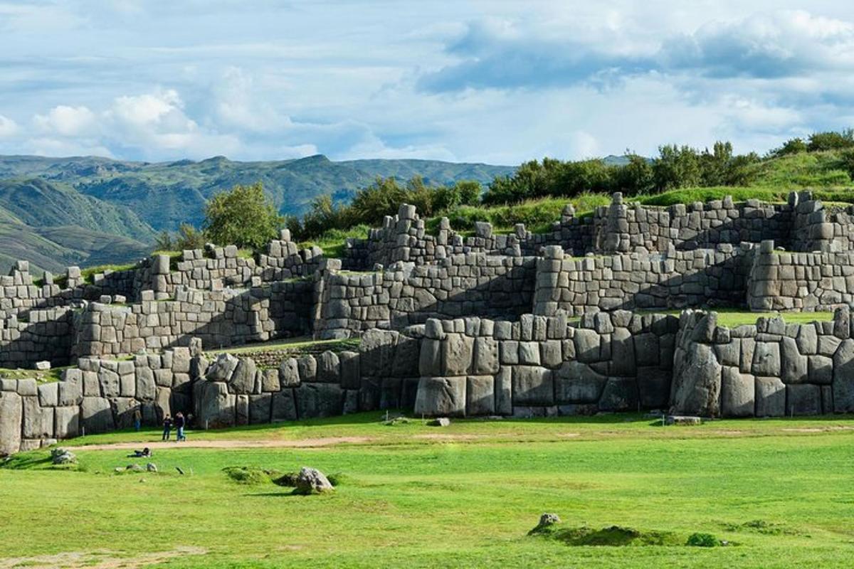 un gran mur de pedra en un camp amb muntanyes al fons