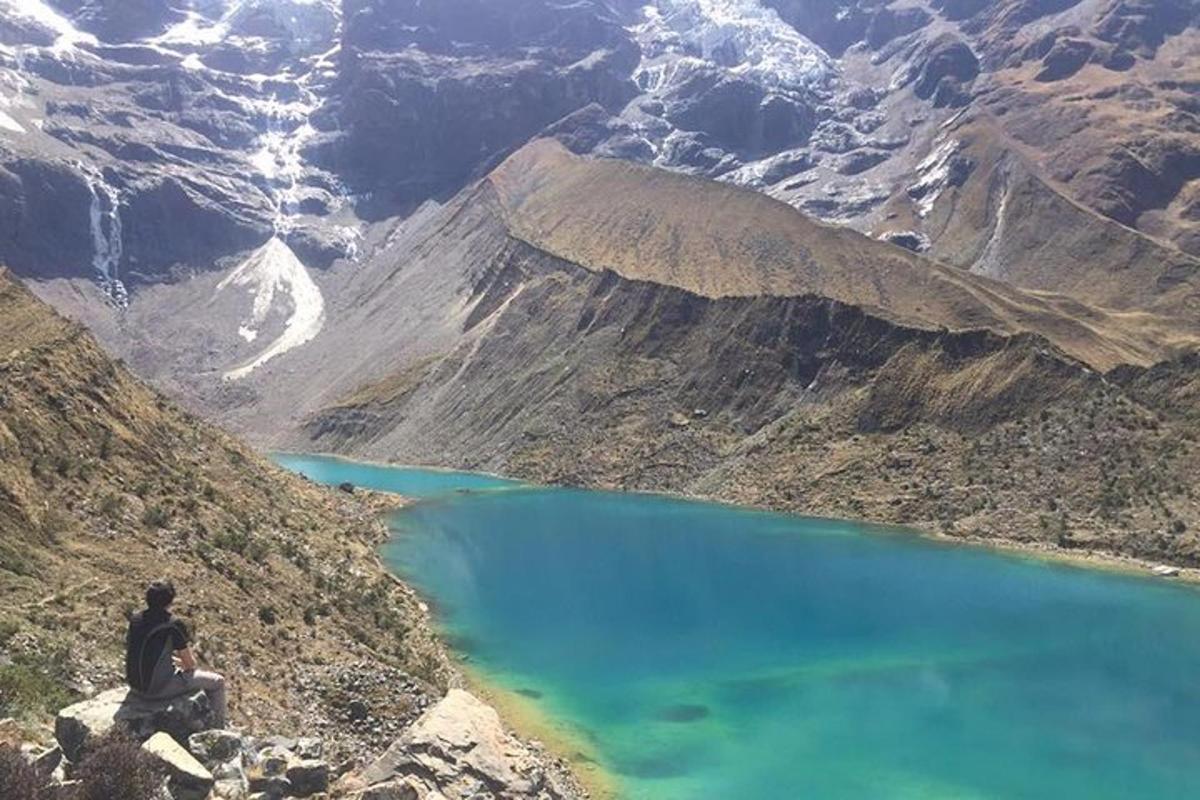 een man zittend op de zijkant van een berg met uitzicht op een blauw meer