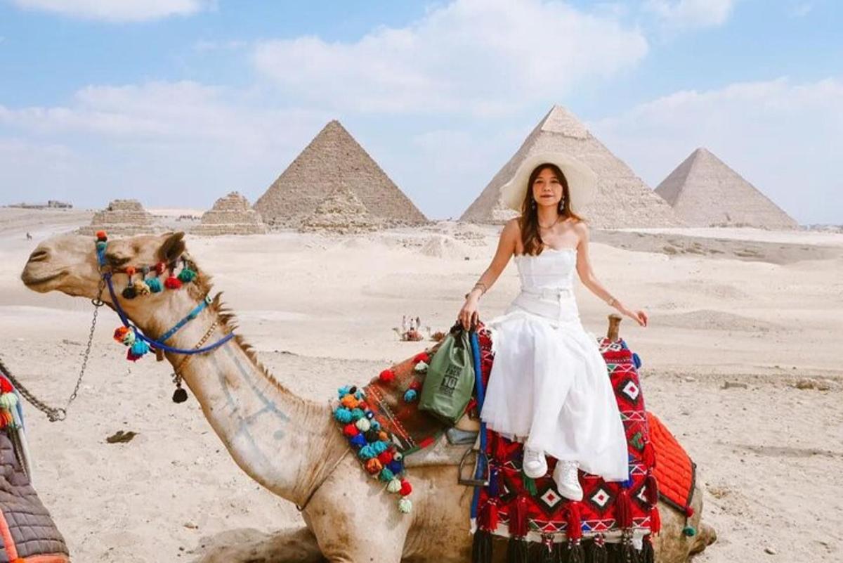 žena jedoucí na velbloudovi před pyramidami