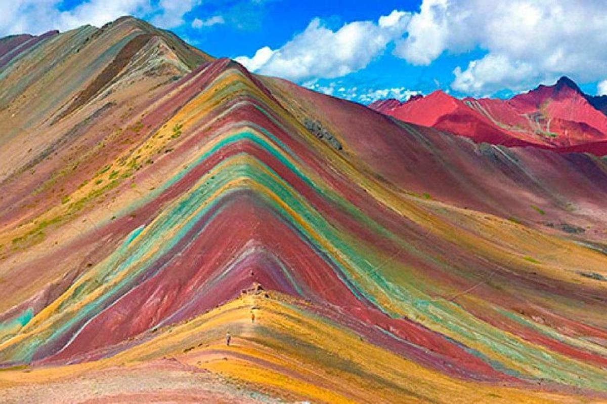 a rainbow colored hill with mountains in the background