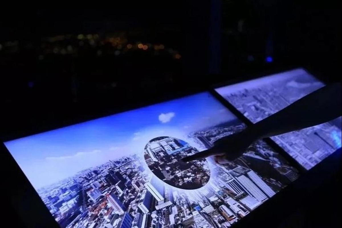 egy kéz mutat egy tévéképernyőre egy várossal