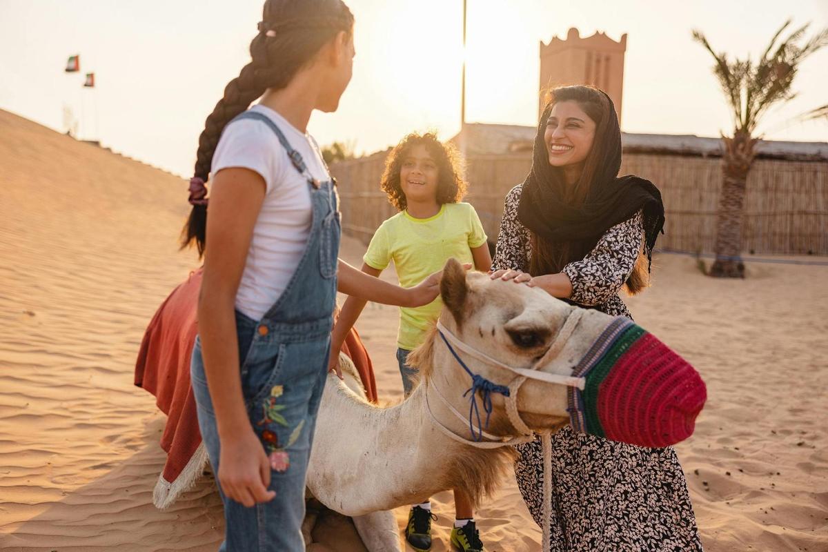 two women and a child petting a camel in the desert