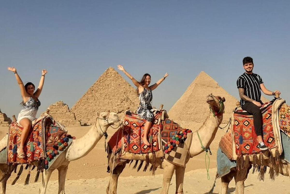 three people riding on camels in front of the pyramids