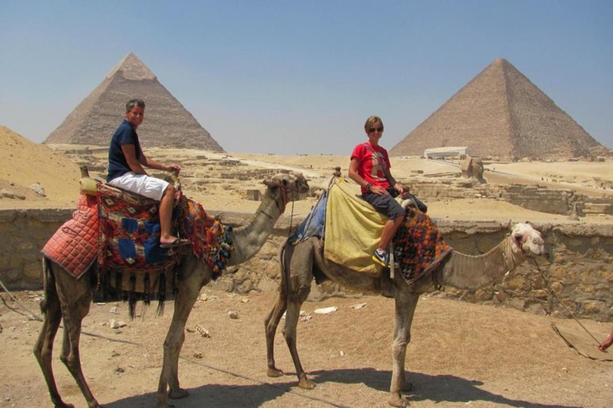 to menn som rir på kameler foran pyramidene