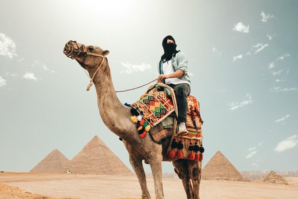 mies ratsastaa kamelilla pyramidien edessä