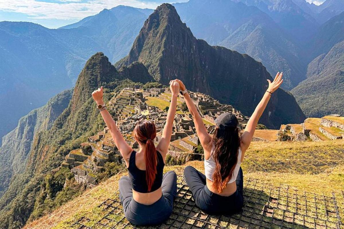 two girls sitting on top of a mountain with their hands in the air