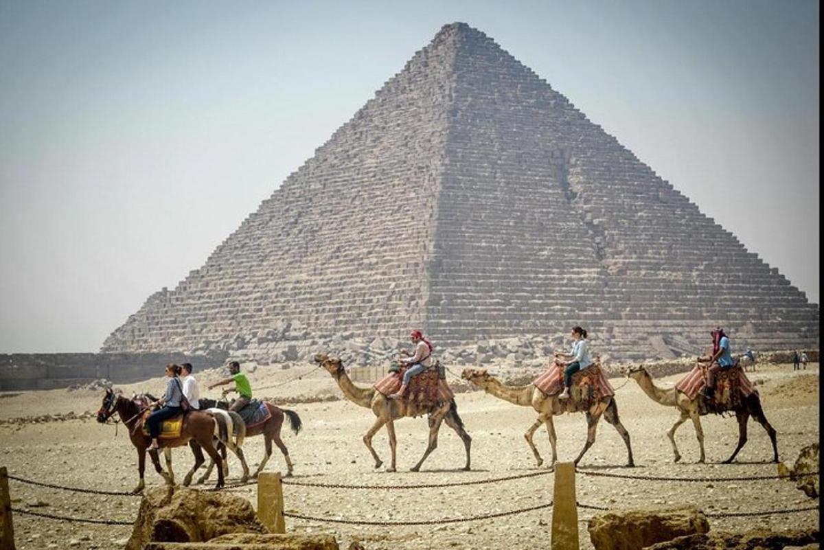 skupina lidí jedoucích na velbloudech před pyramidou