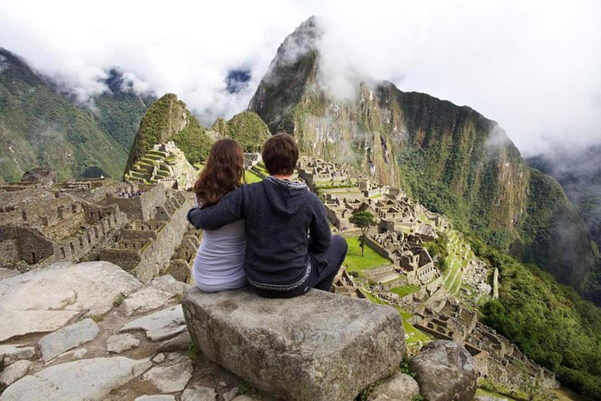 a couple sitting on a rock looking at machu picchu
