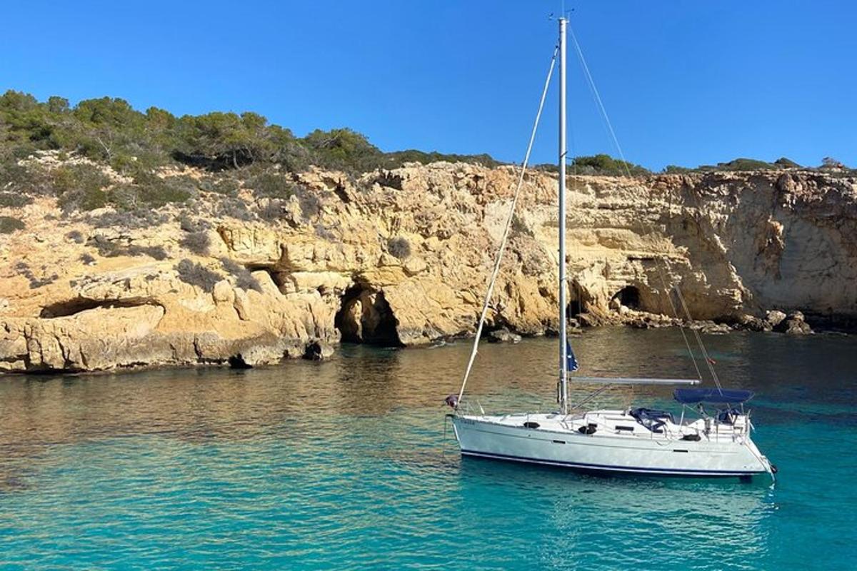 una barca a vela bianca in acqua accanto a una scogliera