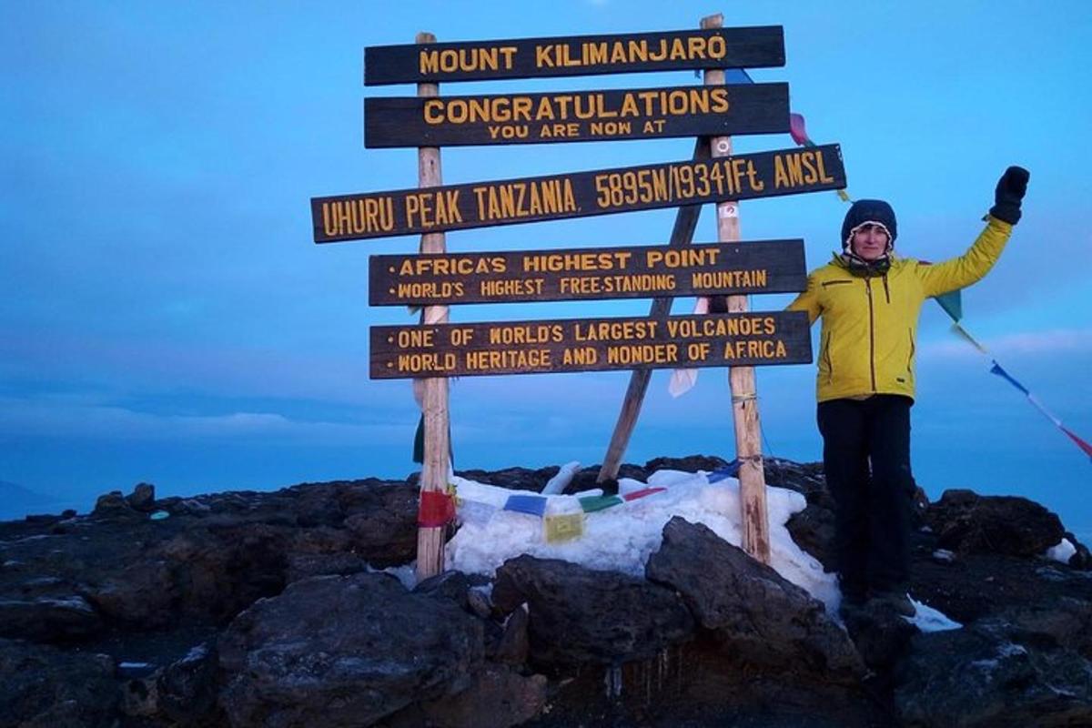 um homem parado ao lado de uma placa no topo de uma montanha