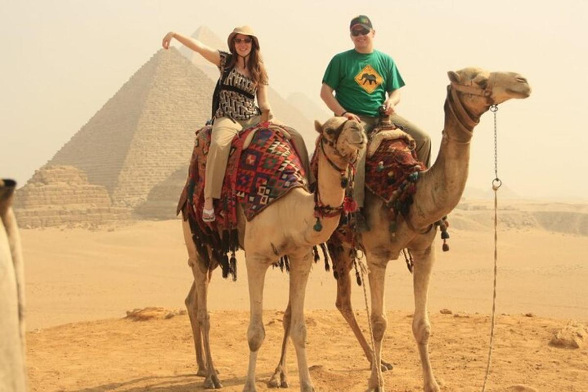 dvaja ľudia jazdiaci na ťavách pred pyramídami
