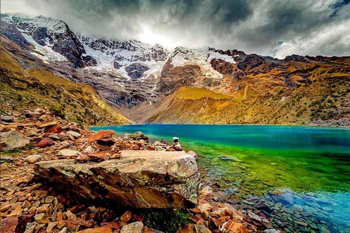 uma pessoa sentada em uma rocha perto de um lago na montanha