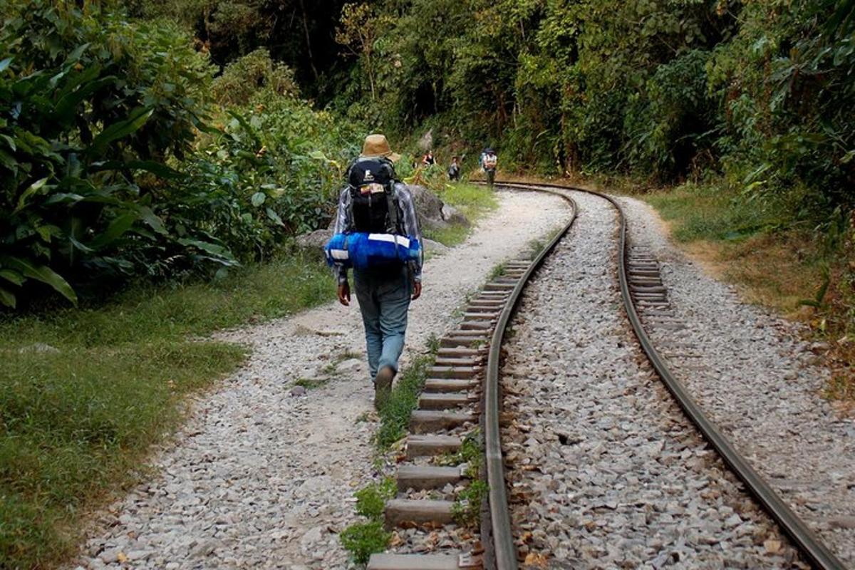 seseorang berjalan menyusuri rel sambil membawa ransel