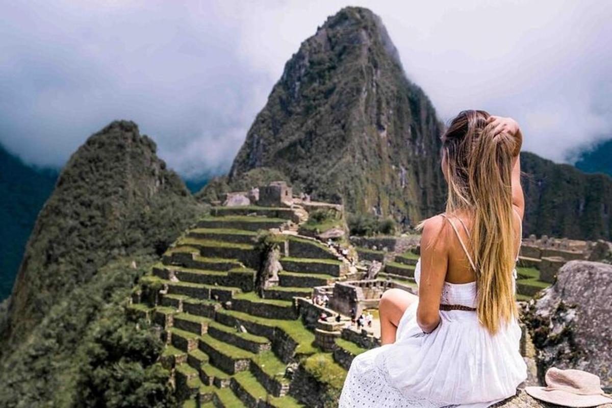 a woman sitting on the edge of a mountain looking up at the ruins