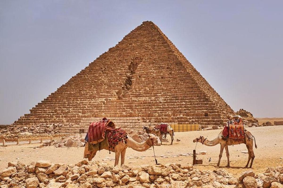 Dos personas en camellos frente a una pirámide