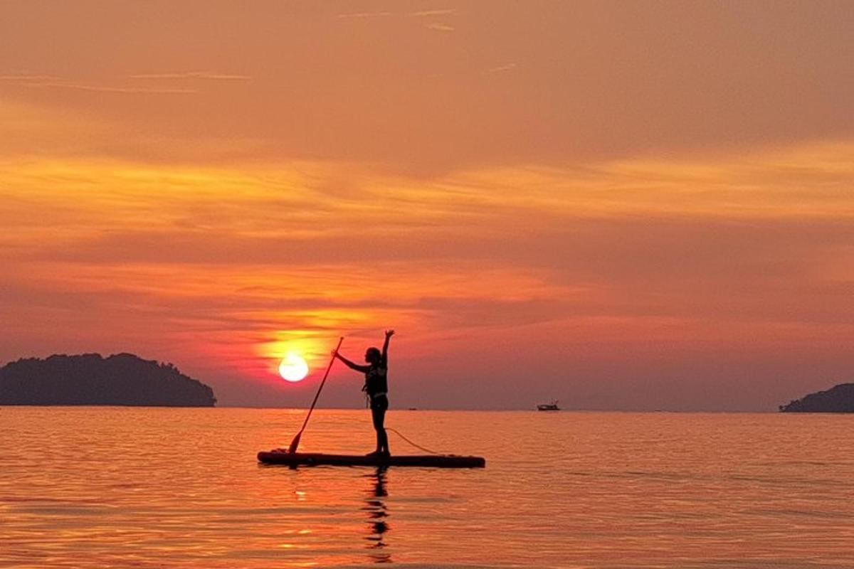 osoba na paddleboardu v oceánu při západu slunce