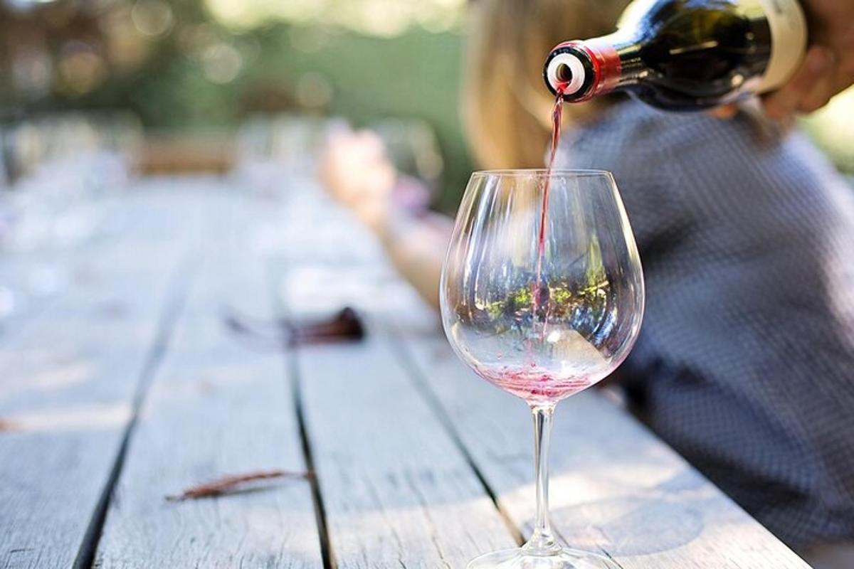 osoba nalewająca wino do kieliszka na drewnianym stole