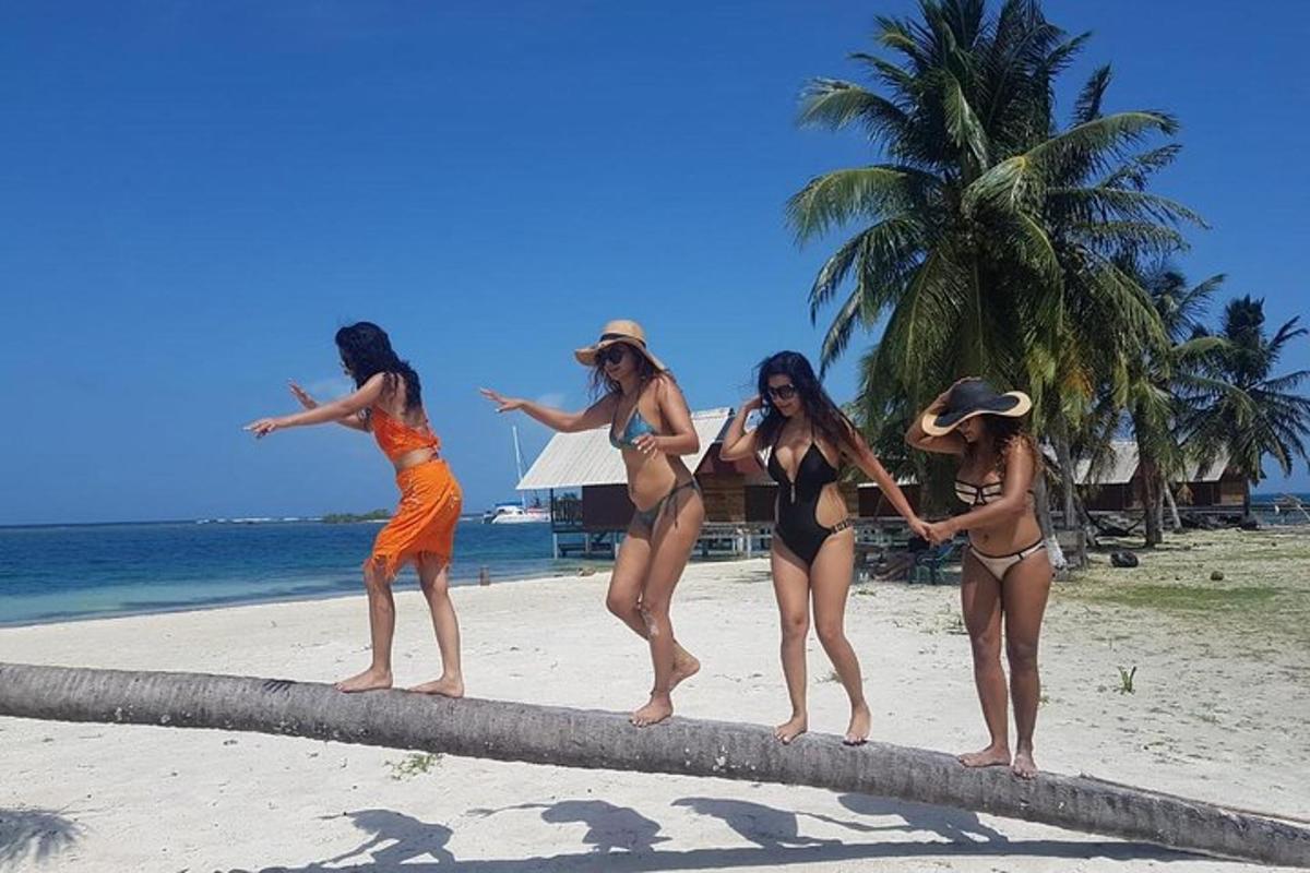 vier Frauen in Badeanzügen stehen auf einem Baumstamm am Strand