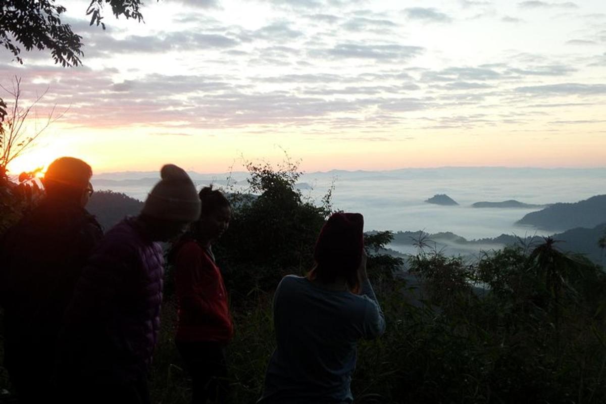 a group of people standing on a hill watching the sunset