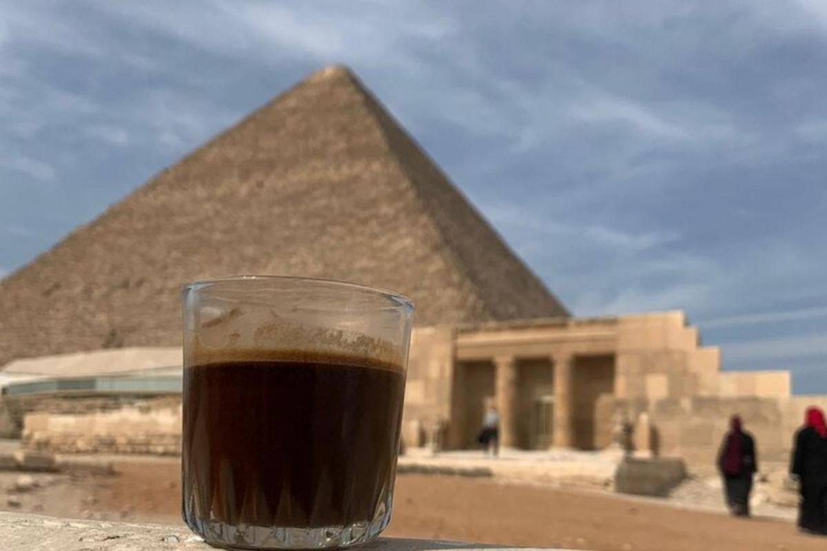segelas kopi duduk di atas meja di hadapan piramid