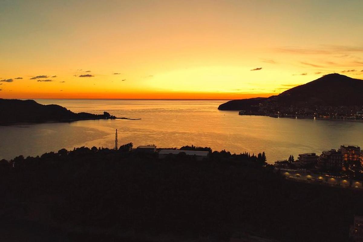 una posta de sol sobre una massa d'aigua amb una ciutat