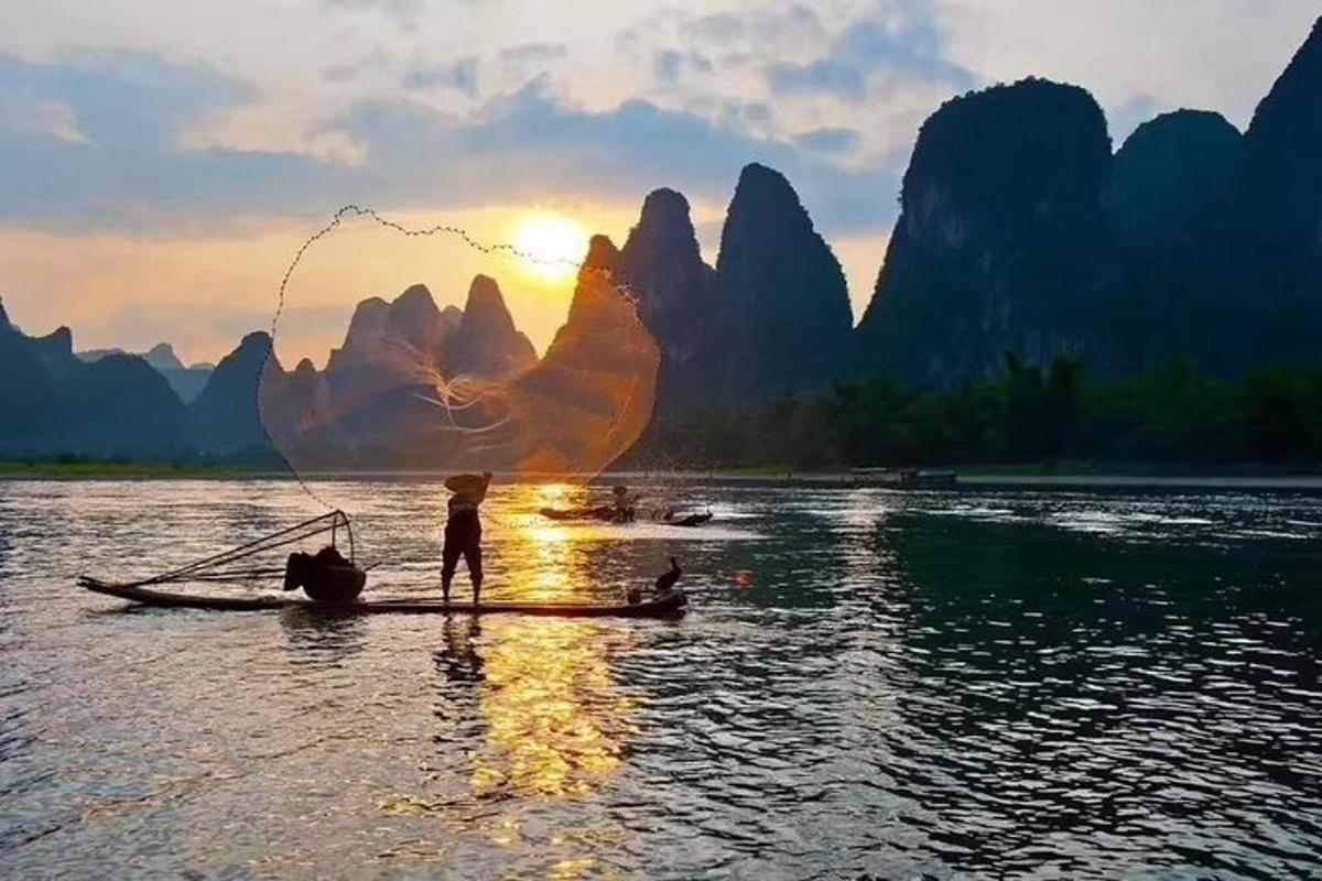 a person fishing on a boat in the water with mountains in the background