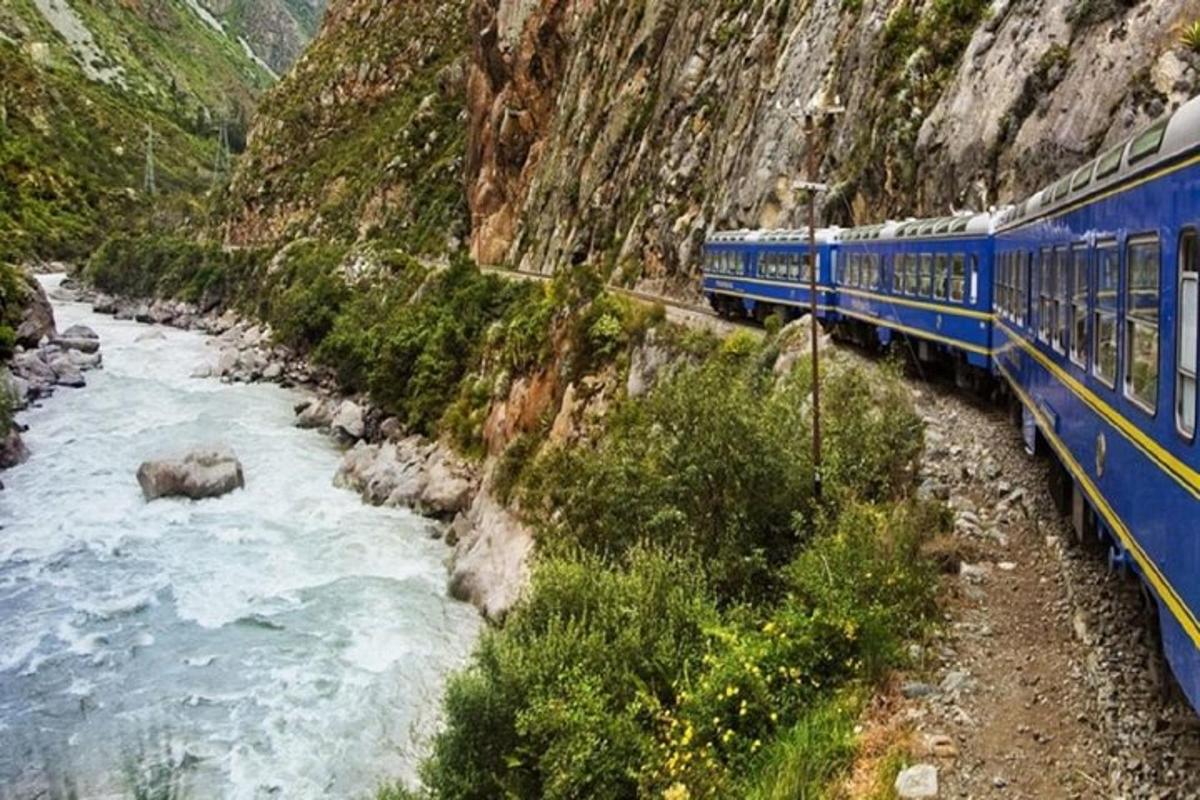 un treno blu che viaggia lungo un fiume accanto a una montagna