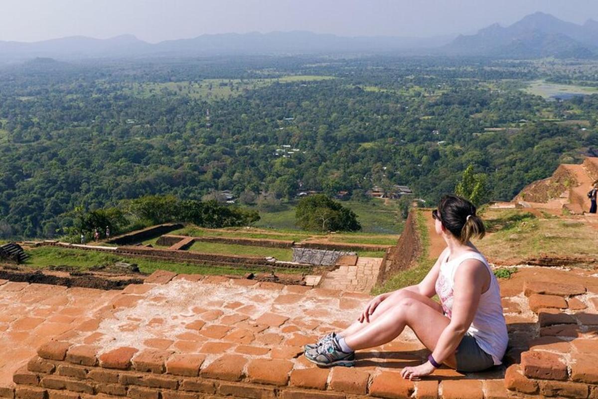 una donna seduta sul bordo di un muro di mattoni che guarda verso una valle