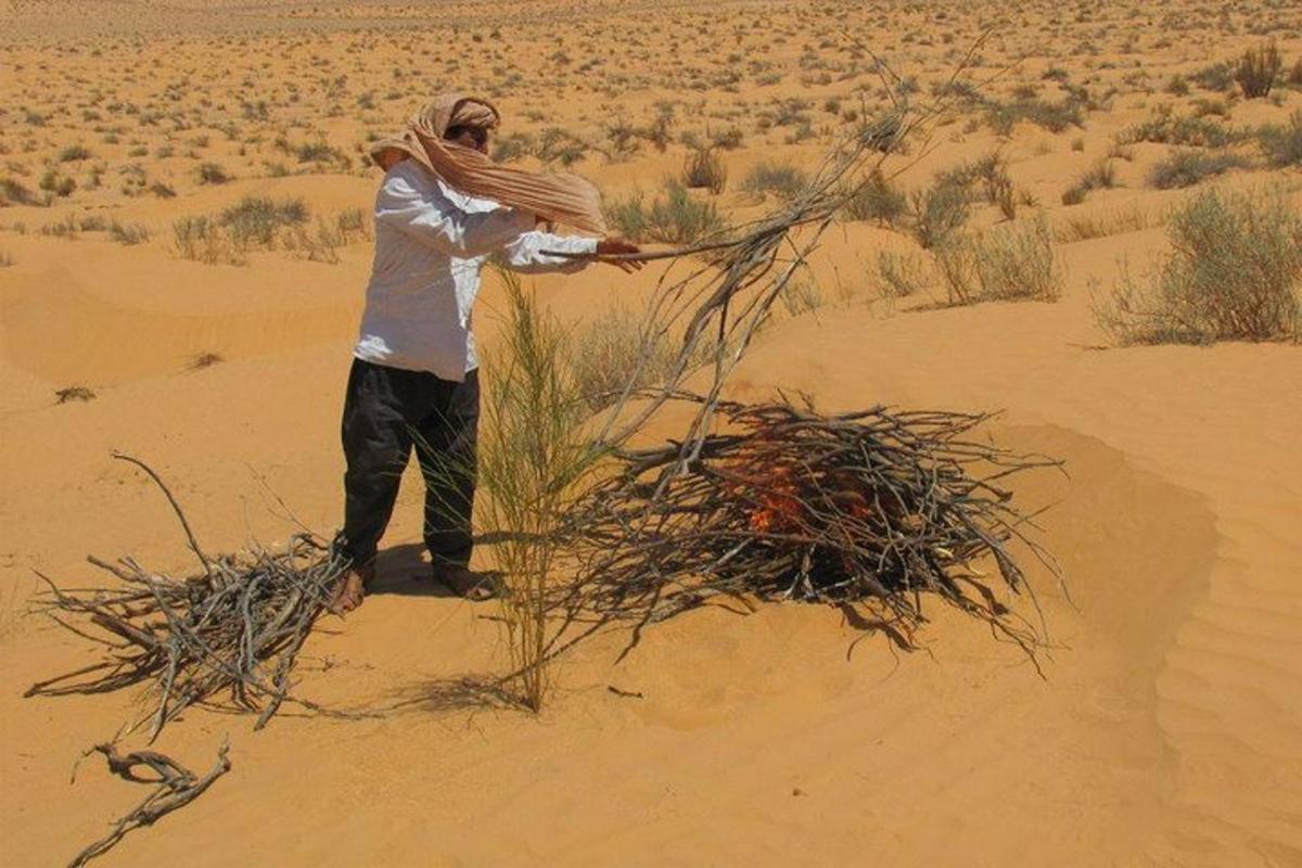 a man standing in the desert with a pile of sticks