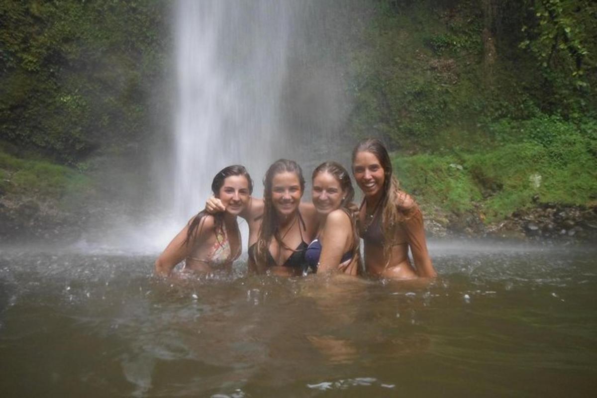 four girls in the water in front of a waterfall