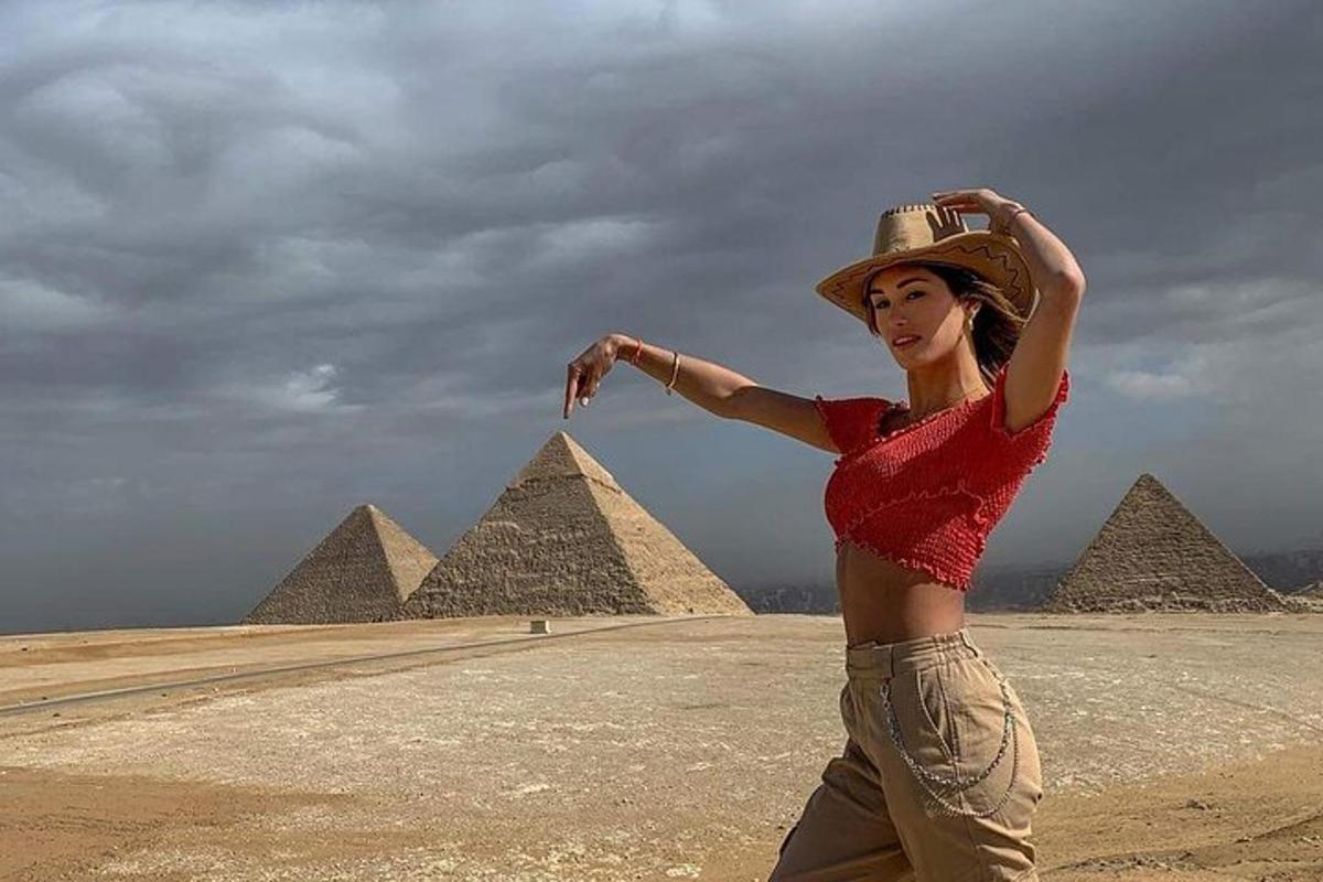 seorang wanita memakai topi berdiri di hadapan piramid