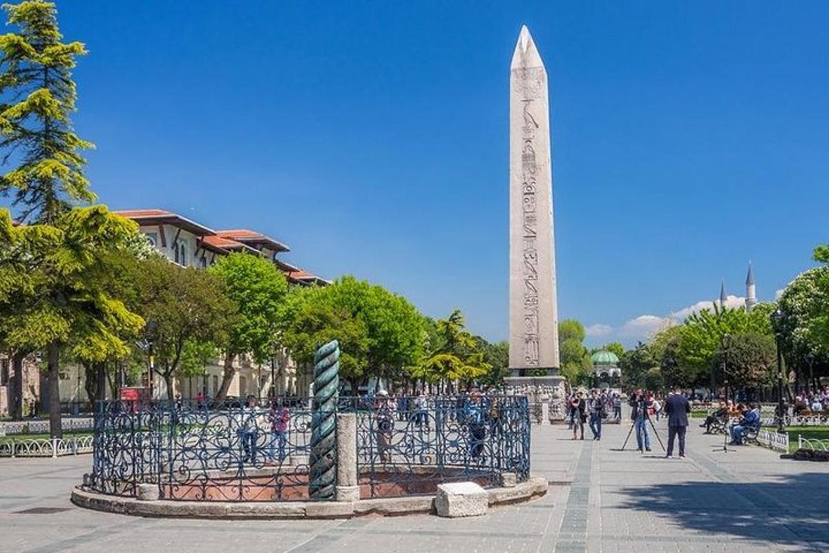 Obelisk í almenningsgarði með minnismerki í bakgrunni