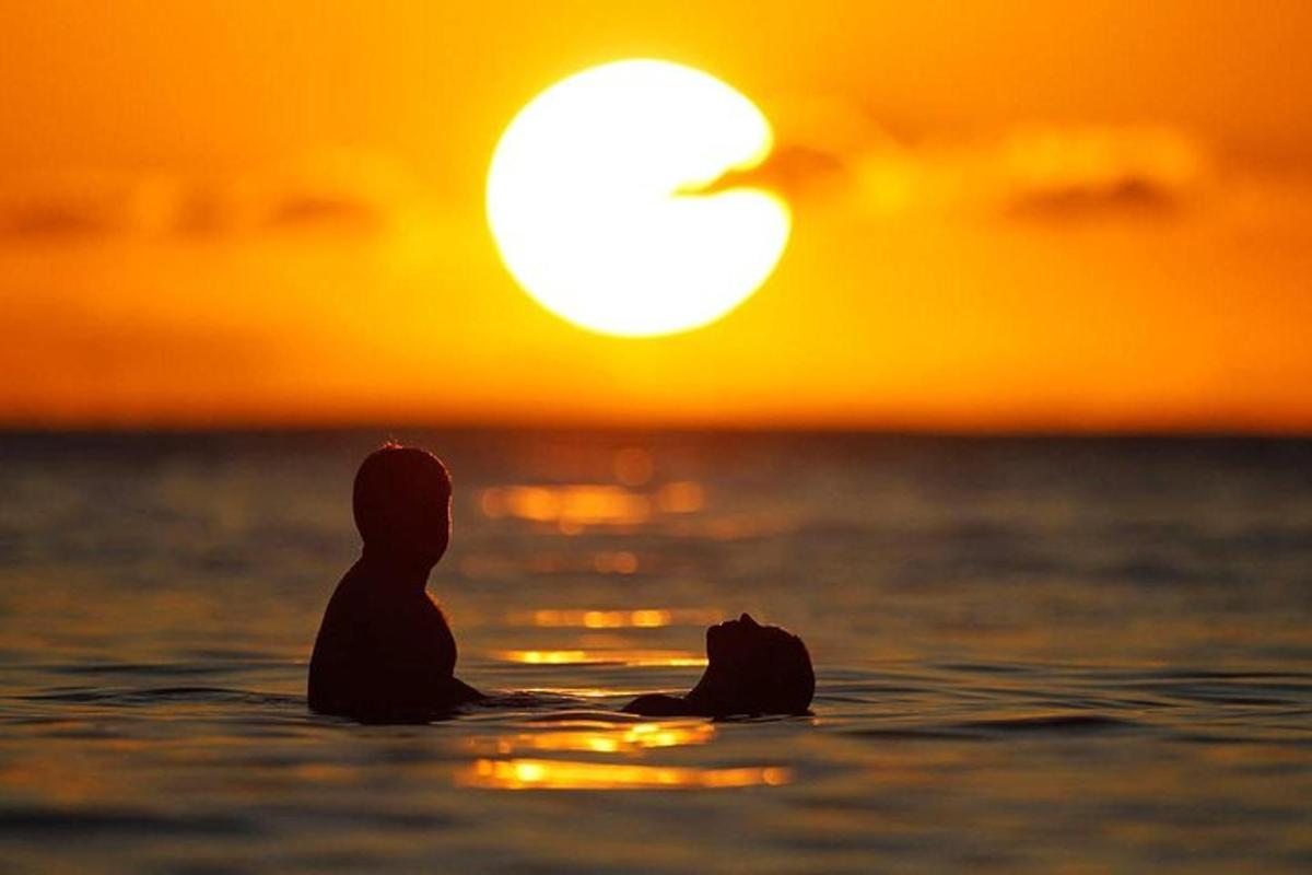 člověk sedící v oceánu a pozorující západ slunce