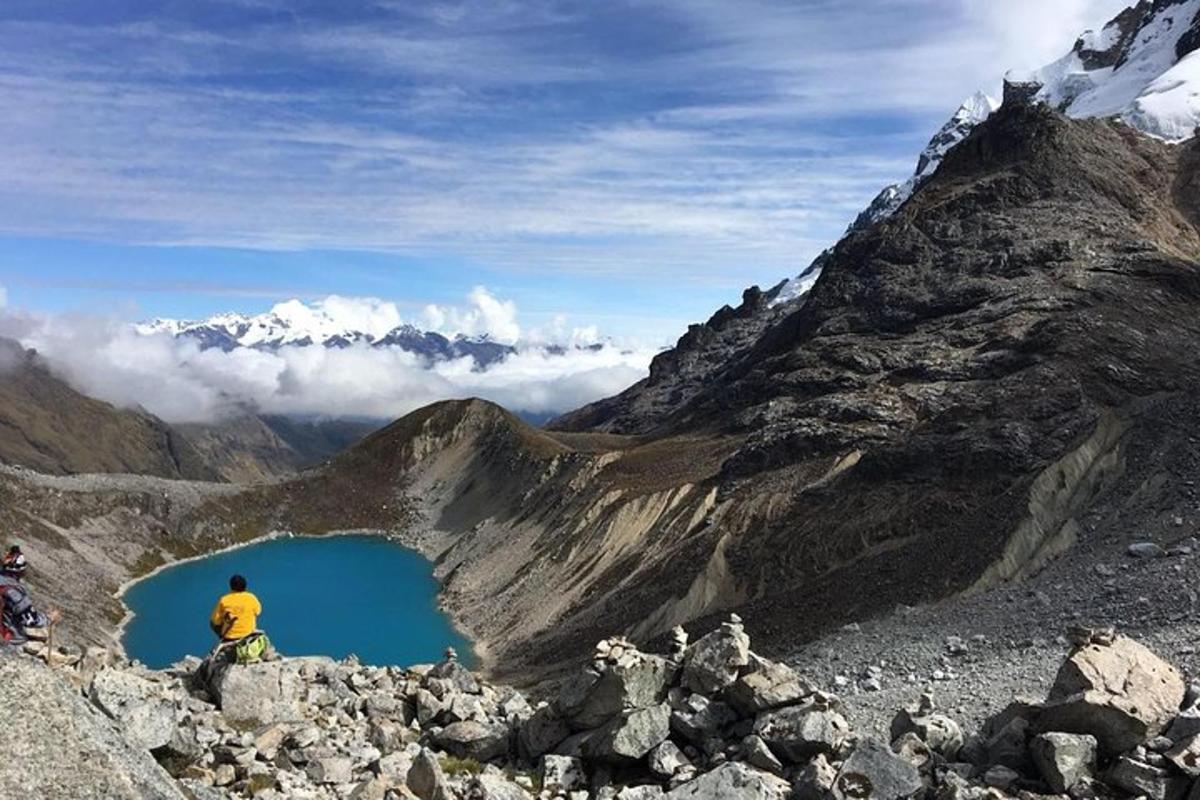 un home assegut al cim d'una muntanya amb vistes a un llac blau