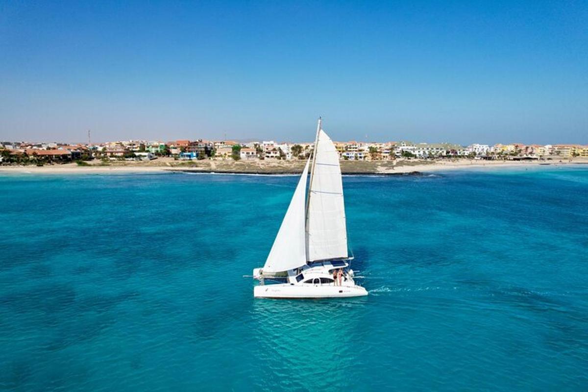 een witte zeilboot in het water met een stad op de achtergrond