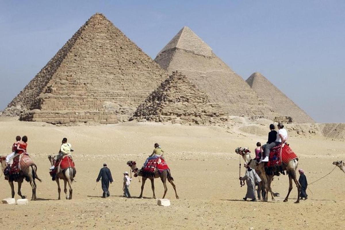 Un grupo de personas en camellos frente a las pirámides.