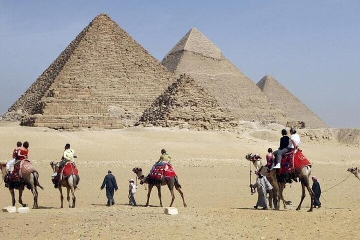 Skupina lidí na velbloudech před pyramidami