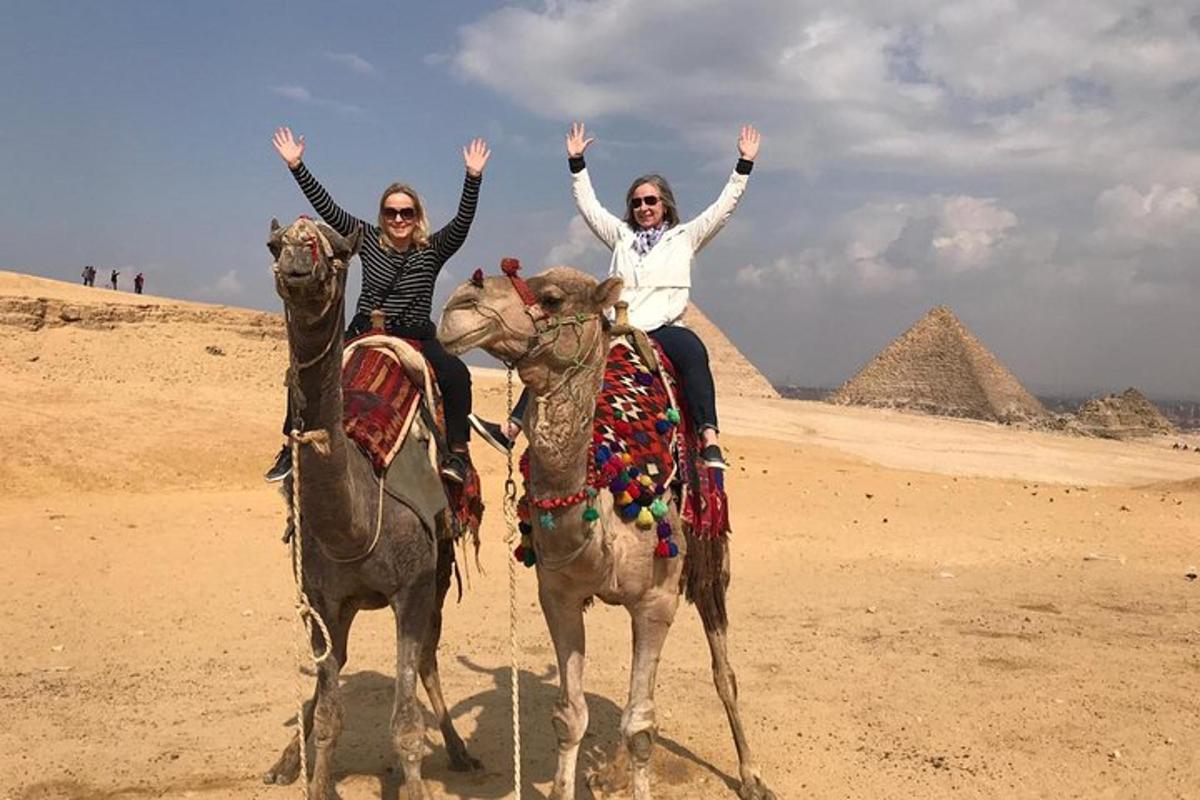 Dos mujeres montando camellos frente a las pirámides