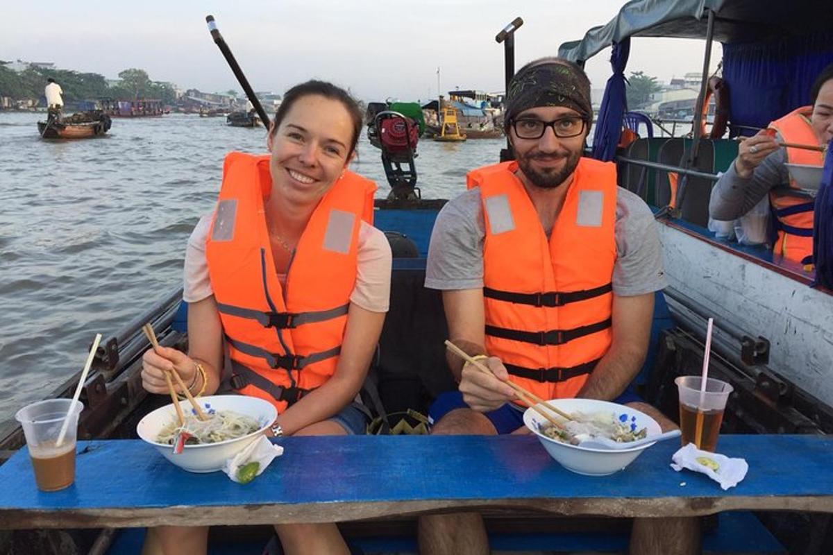 two people in orange life vests eating food on a boat
